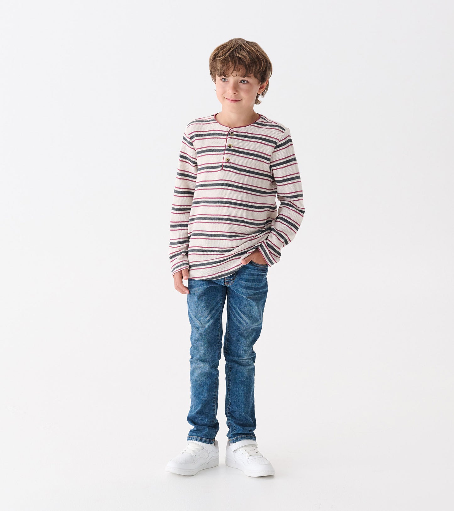 Boys' long-sleeve henley in oatmeal melange with colorful stripes, paired with blue jeans and white sneakers.