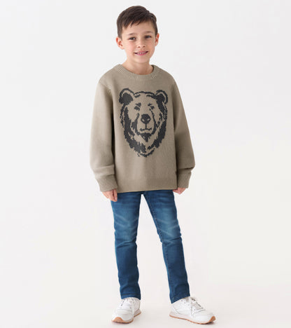 Oatmeal crew neck sweater featuring a bear graphic, paired with blue jeans and white sneakers.