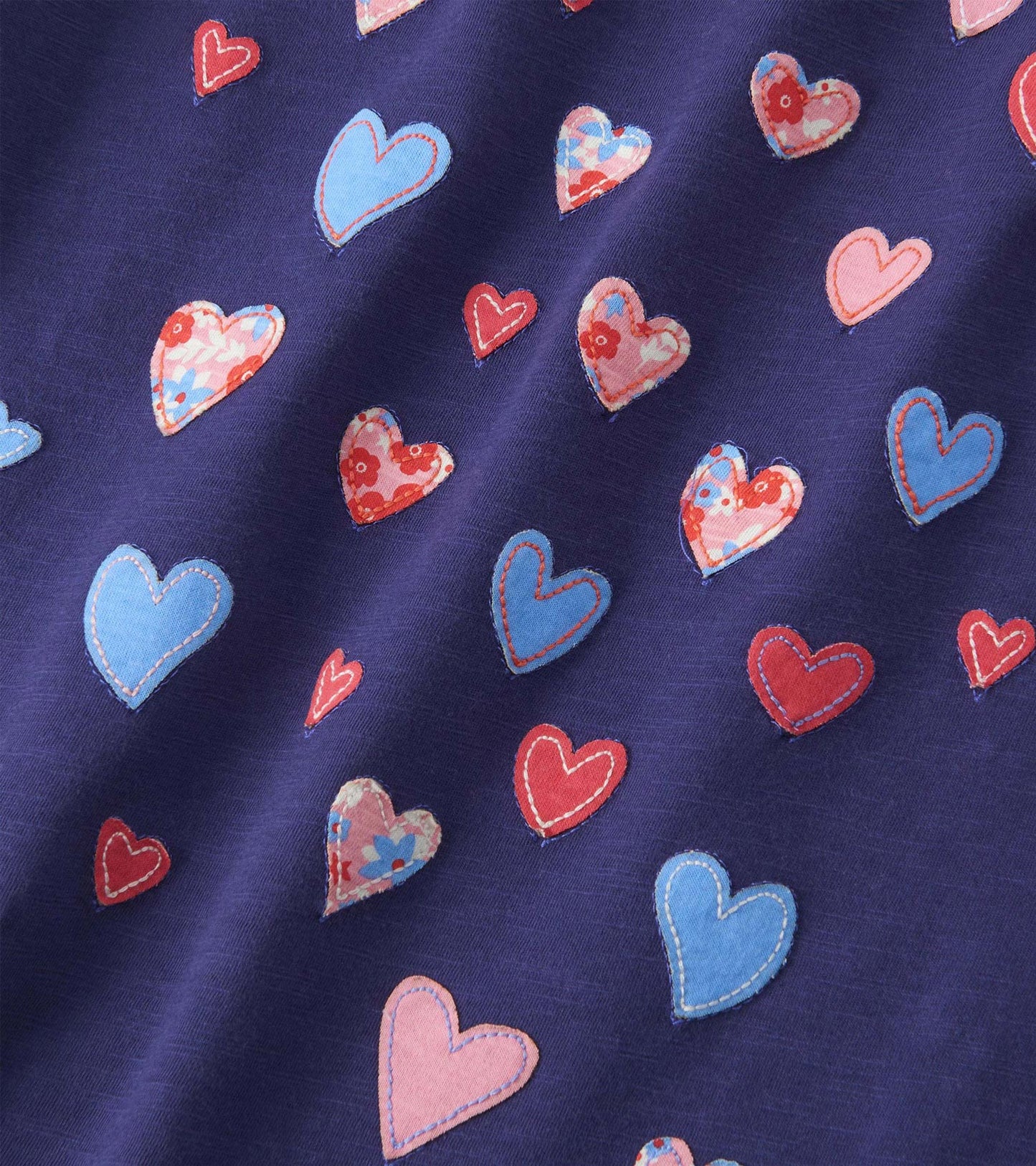 Navy long sleeve tee featuring colorful, patterned hearts in various sizes and shapes. Soft fabric with a casual design.