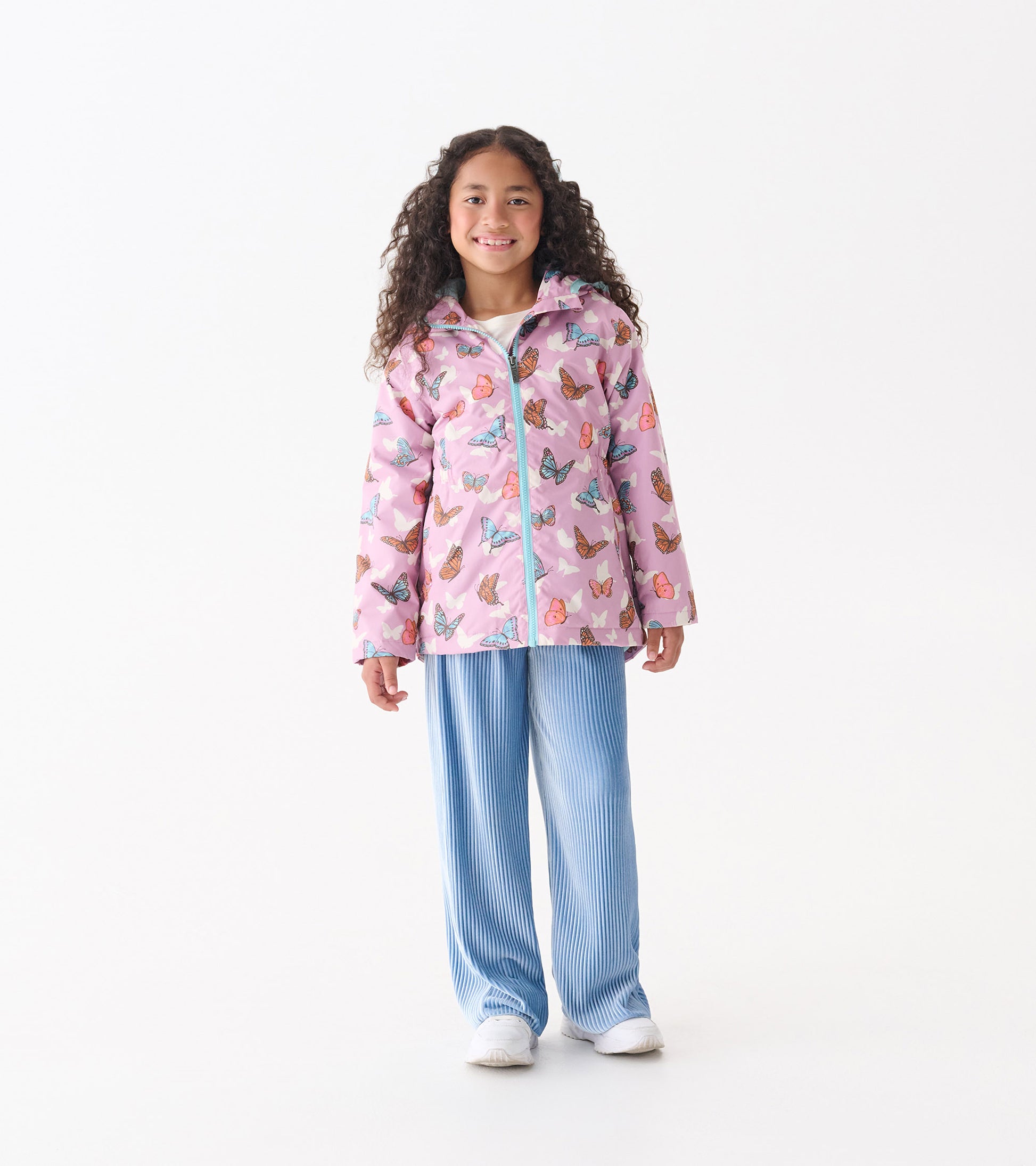 Lightweight pink rain jacket with colorful butterfly print, featuring a zip-up front and hood, worn over blue striped pants.