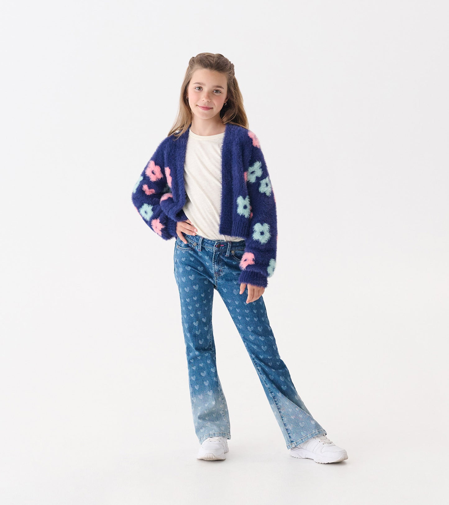 Navy open cardigan with big pastel flowers, paired with a white shirt and flared jeans, worn by a girl.