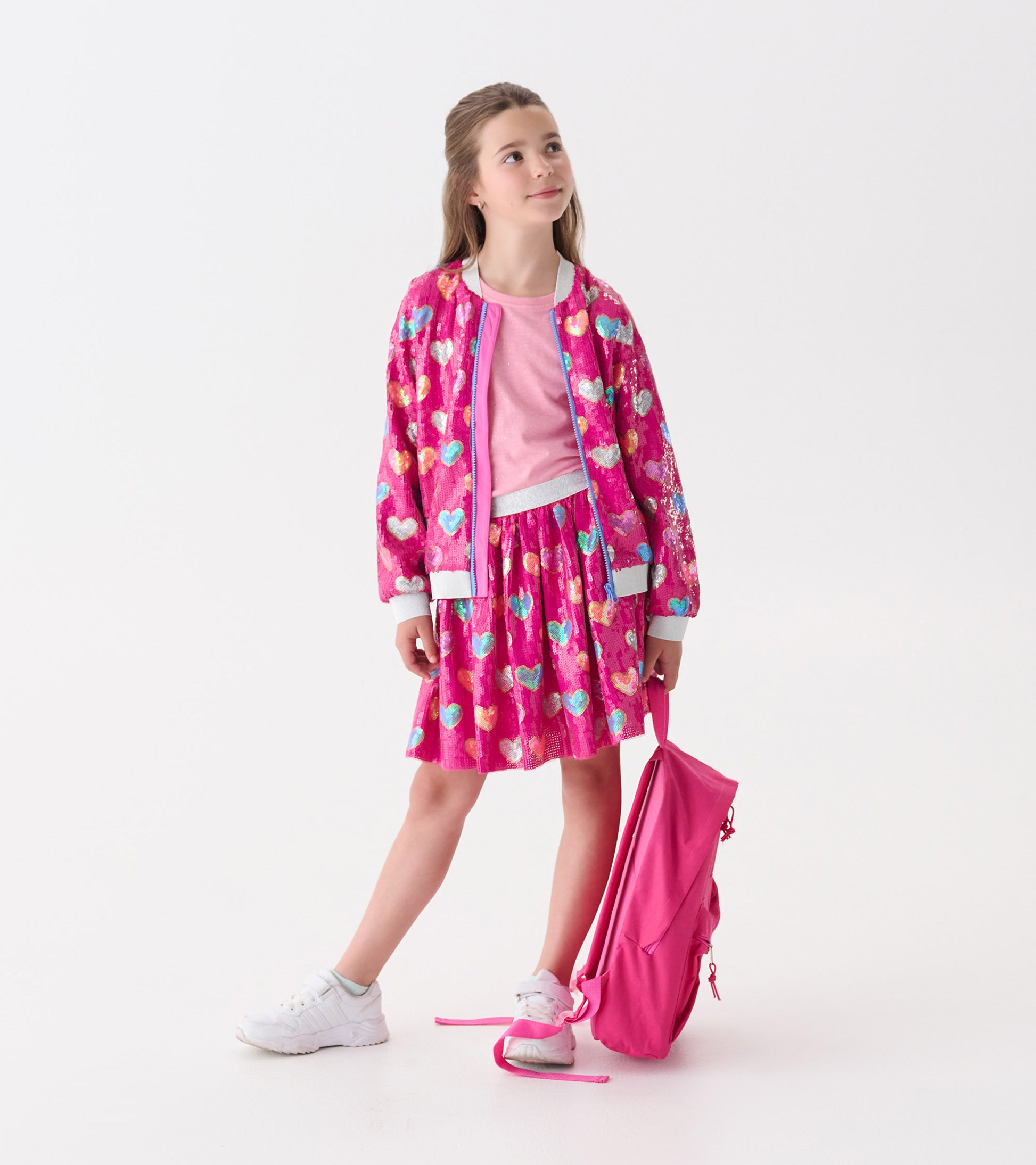 Pink bomber jacket with sequin heart pattern, paired with a pink top and skirt, worn by a girl holding a pink backpack.
