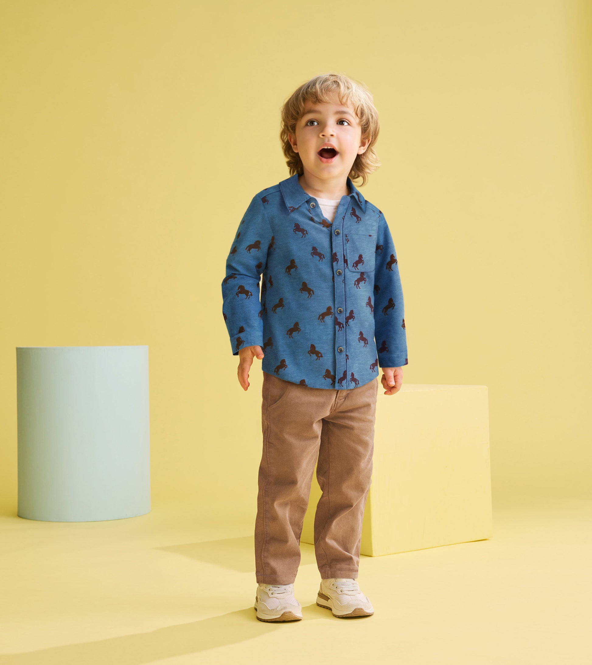 Blue button-down shirt with horse print, worn by a toddler, paired with beige pants, against a yellow background.