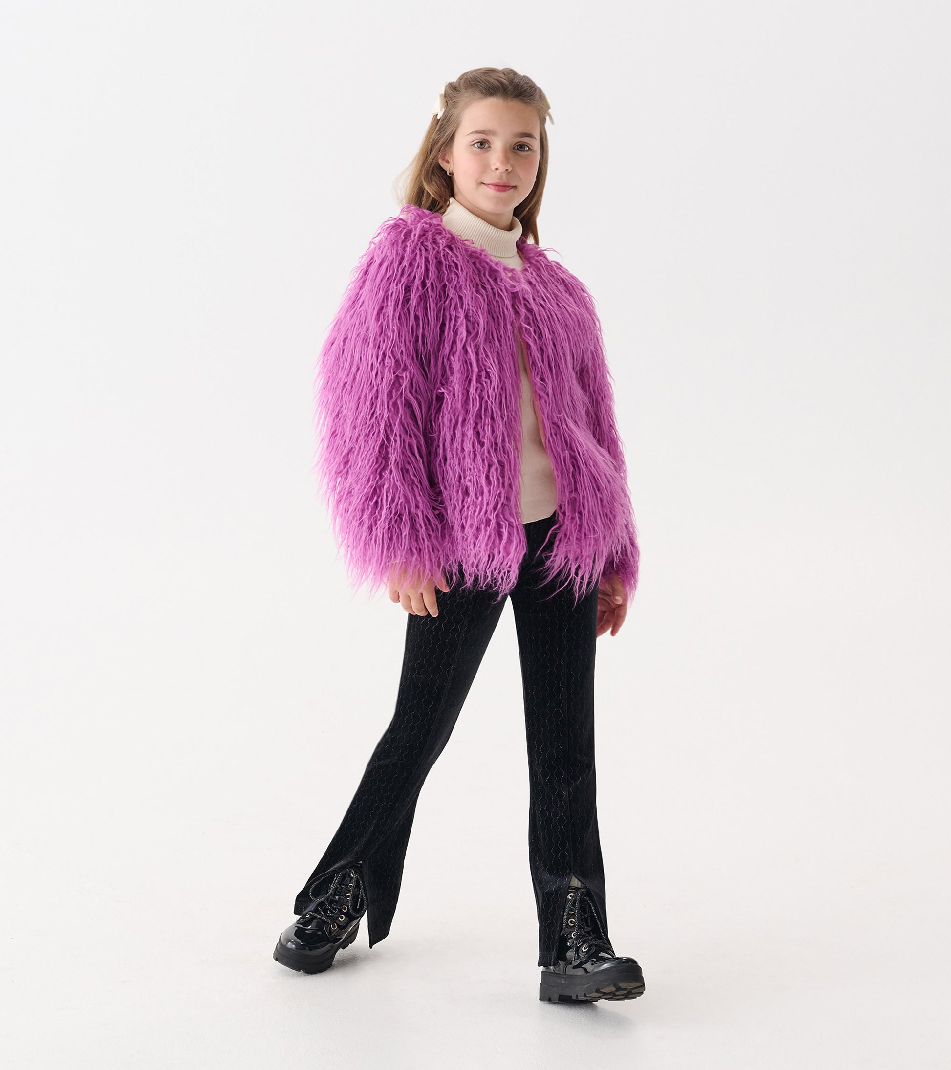 Purple Mongolian faux fur topper with long sleeves, worn over a light sweater and paired with black pants and boots.