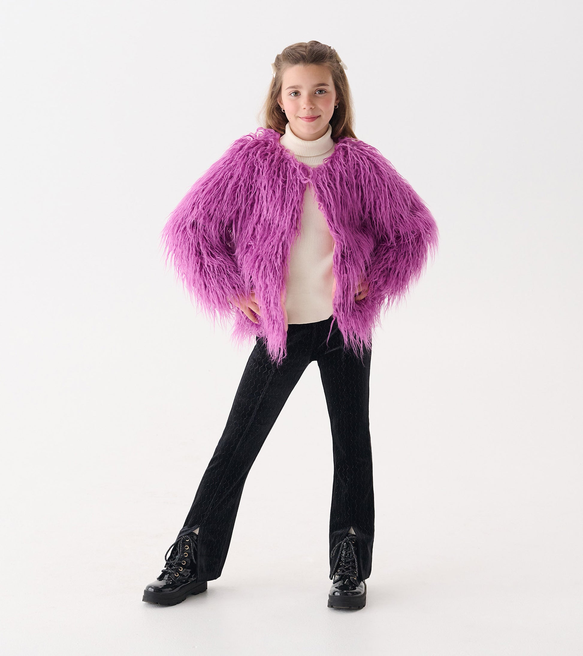 Faux fur topper in radiant orchid color with long, fluffy sleeves, worn over a white turtleneck and black pants.