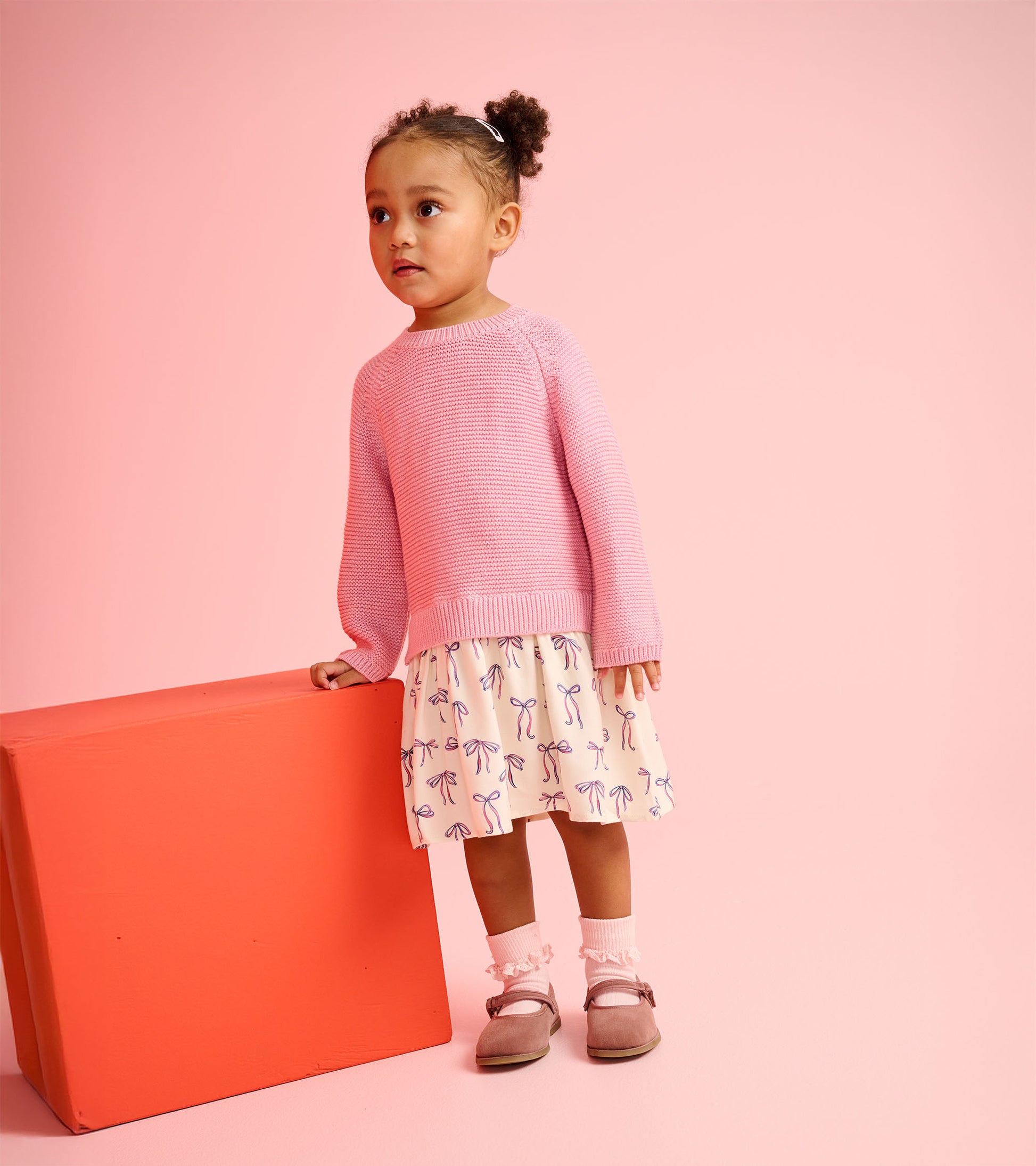Pink knitted sweater paired with a cream skirt featuring painted bows, worn with pink socks and gray shoes.