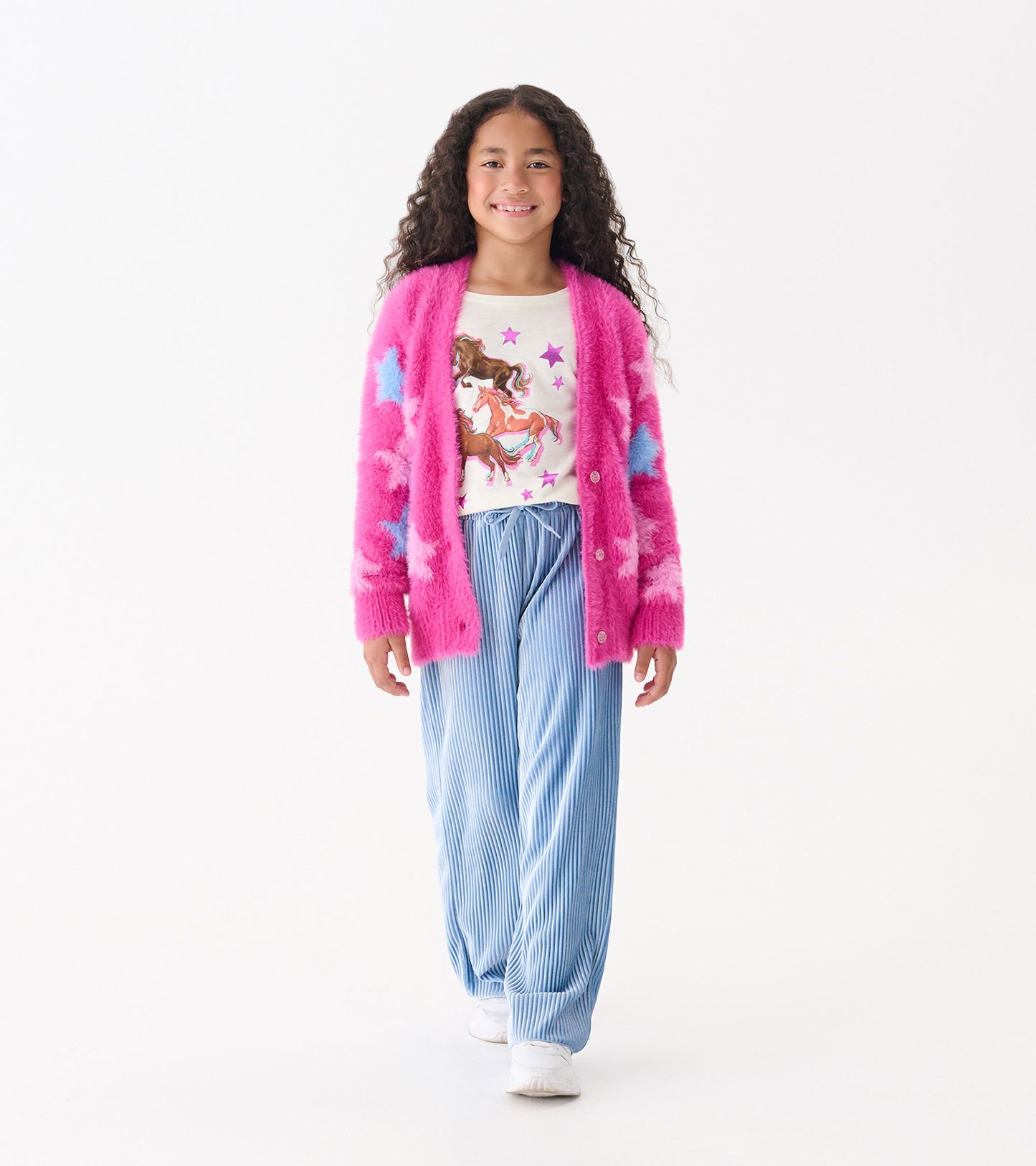 Fuzzy pink cardigan with blue stars, worn over a white graphic tee and paired with blue striped pants.