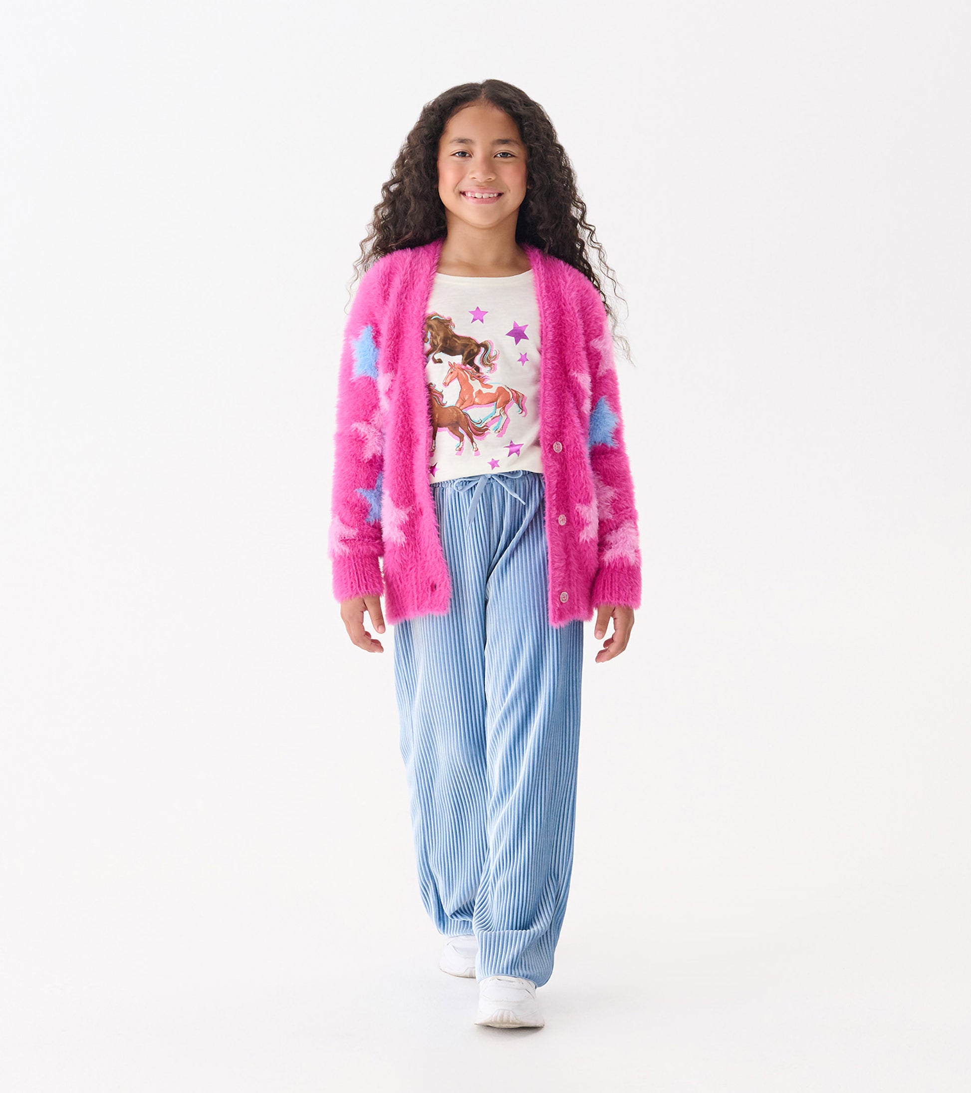 Fuzzy pink cardigan with blue stars, worn over a white graphic tee and paired with blue striped pants.