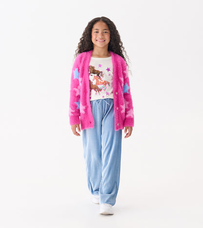Fuzzy pink cardigan with blue stars, worn over a white graphic tee and paired with blue striped pants.