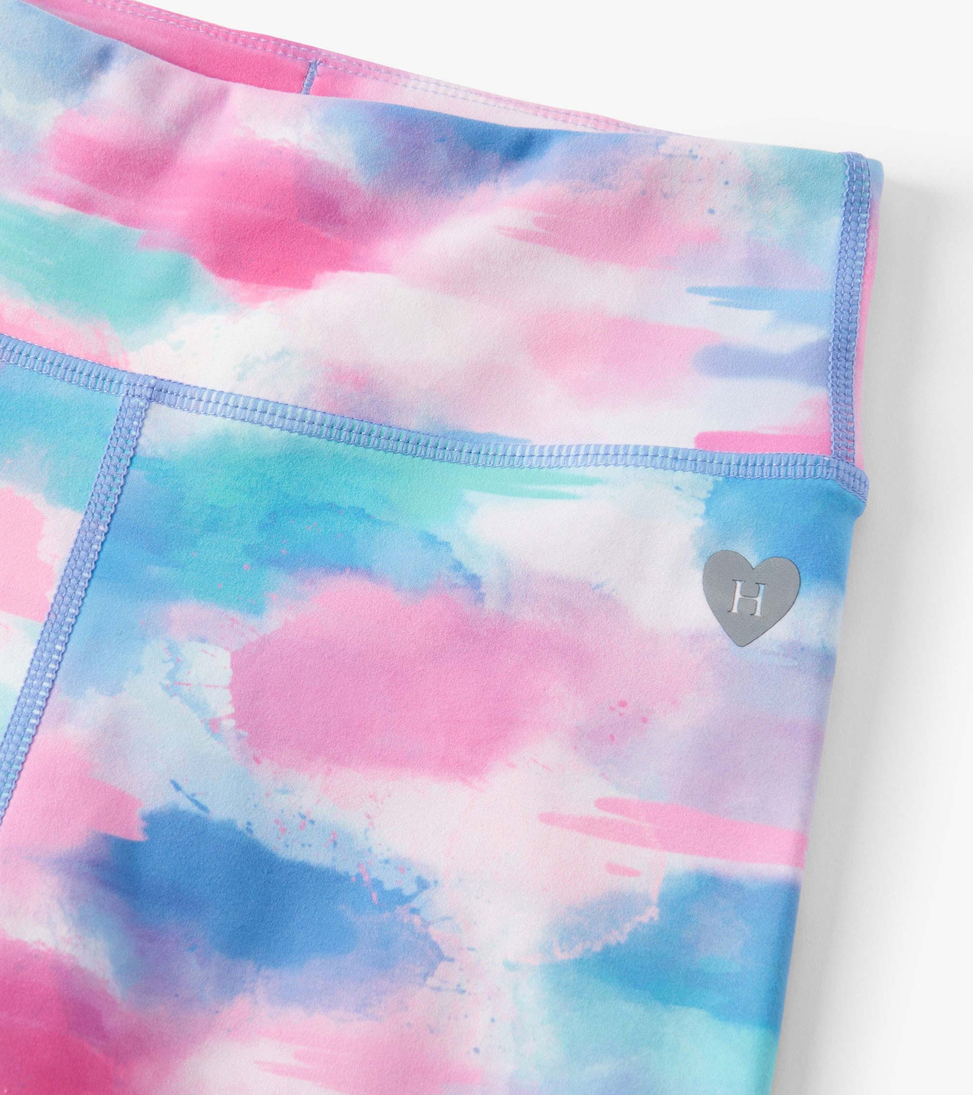 Colorful active leggings featuring a watercolor pattern in pink, blue, and green with a heart logo on the waistband.