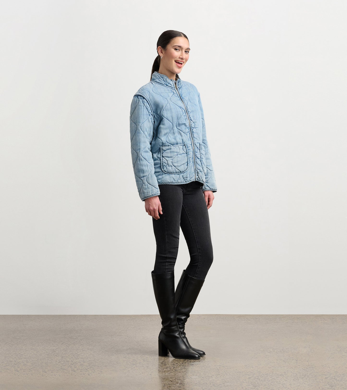 Quilted jacket in washed blue Tencel, featuring a zip front, high collar, and two front pockets, worn with black jeans.