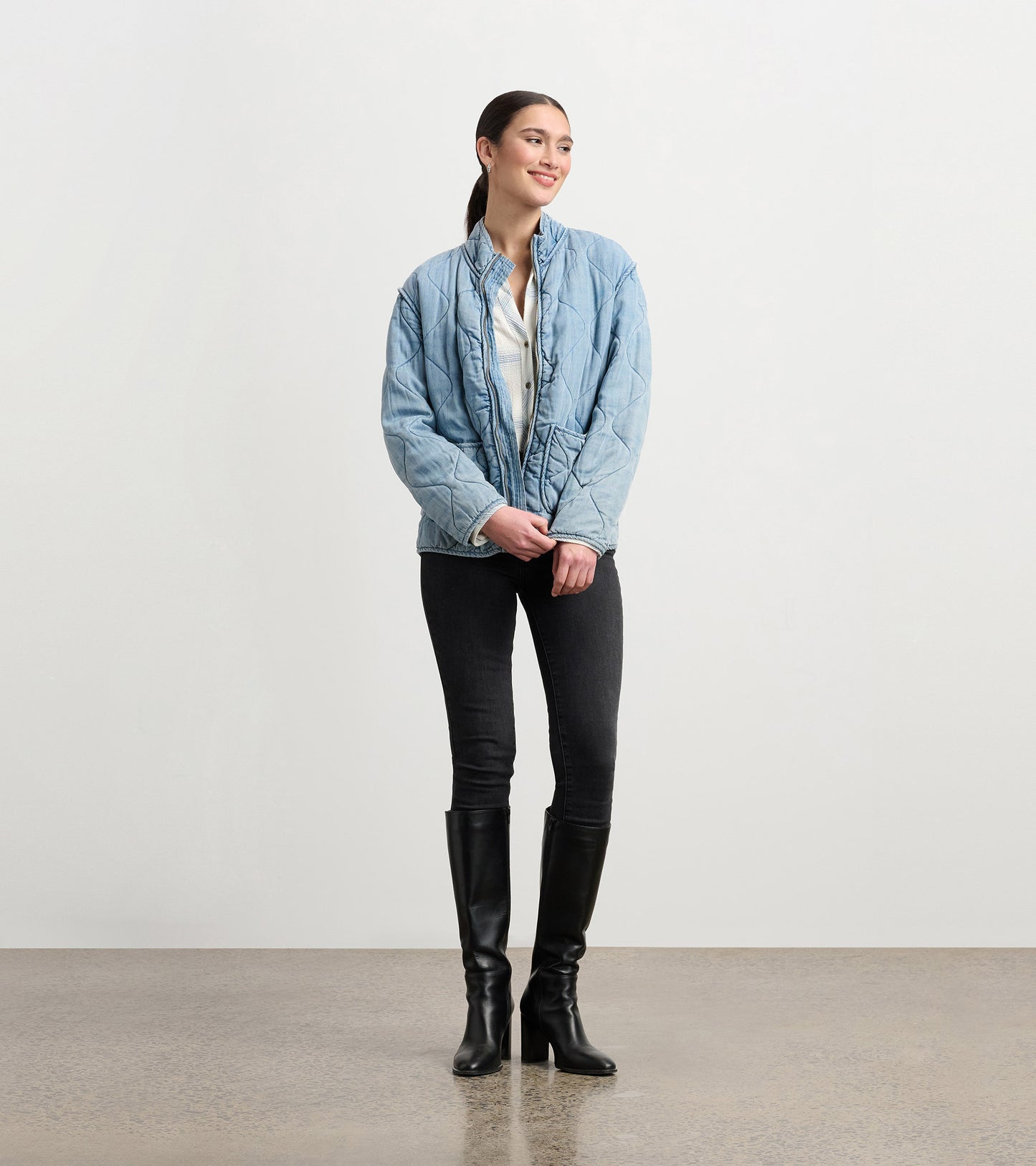 Quilted jacket in washed blue Tencel, featuring a relaxed fit and high collar, styled with black jeans and knee-high boots.