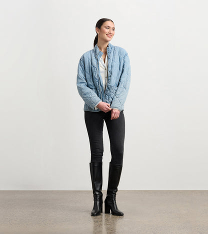 Quilted jacket in washed blue Tencel, featuring a relaxed fit and high collar, styled with black jeans and knee-high boots.