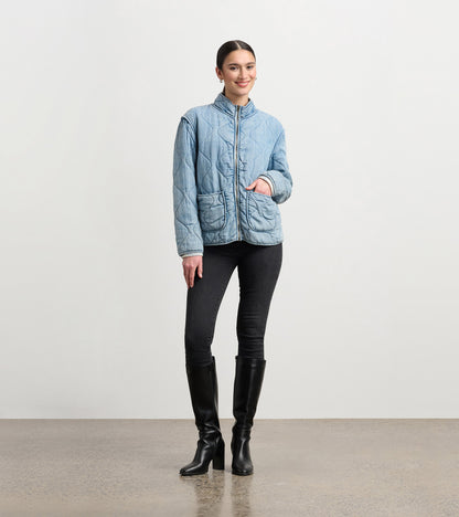 Quilted jacket in washed blue Tencel, featuring a high collar and front pockets, styled with black jeans and boots.