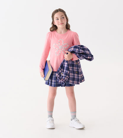 Pink long-sleeve tee with embroidered flower design, paired with a plaid skirt and holding a book and jacket.