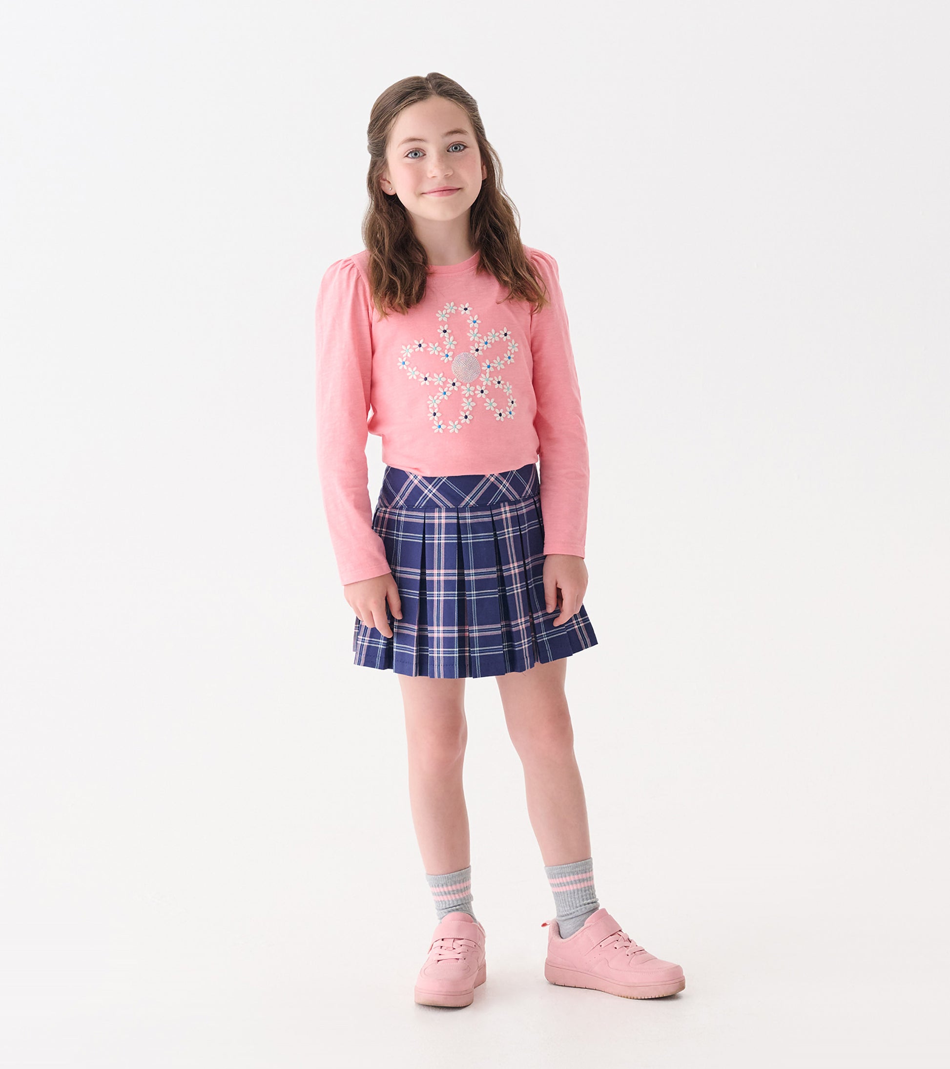 Pink long-sleeve tee with embroidered flower design, paired with a navy plaid skirt and pink sneakers.