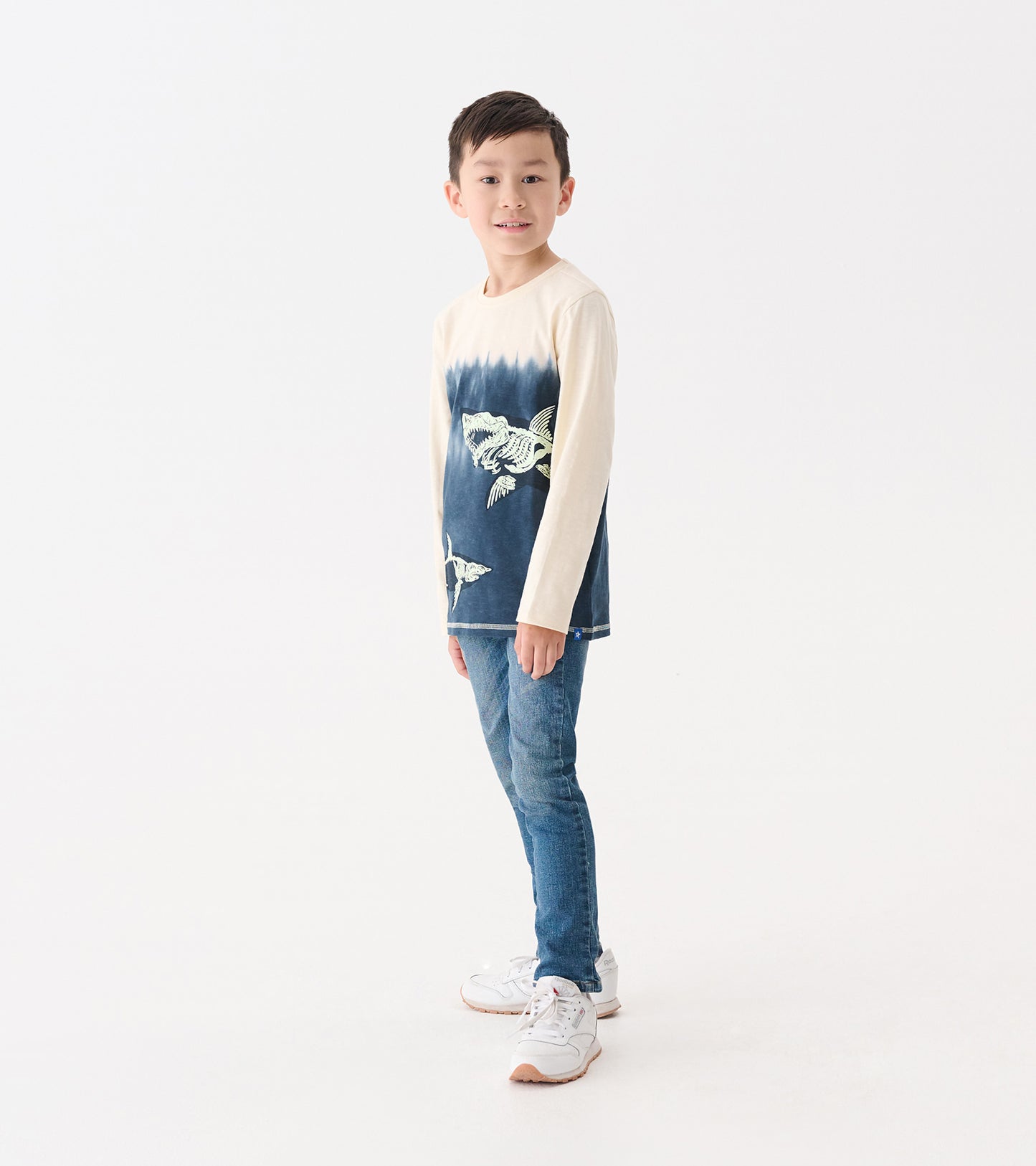 Long sleeve graphic tee featuring a shark design in blue and cream, worn by a boy with jeans and sneakers.