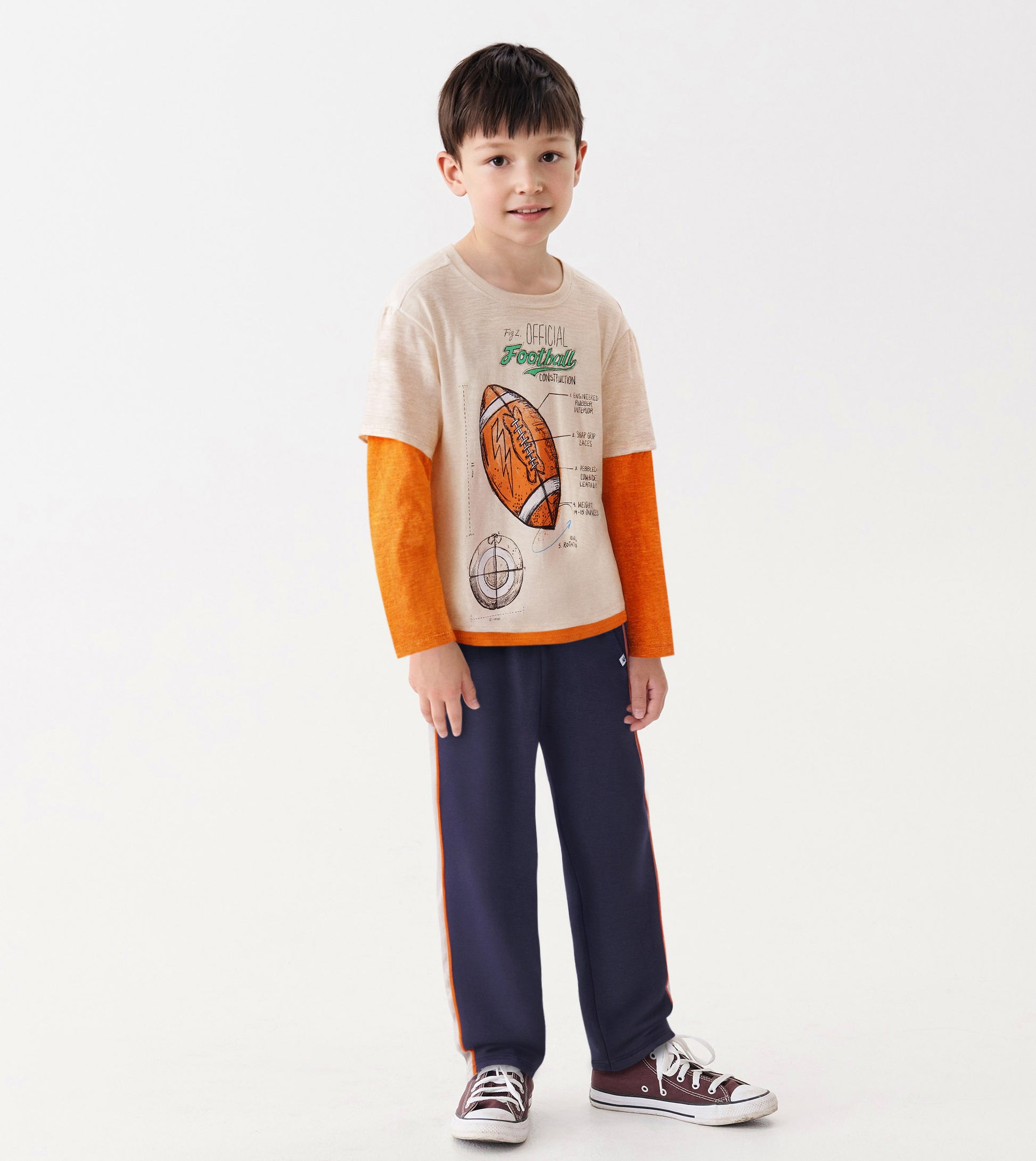 Long sleeve t-shirt featuring a football graphic, beige body, and orange sleeves, paired with navy pants.