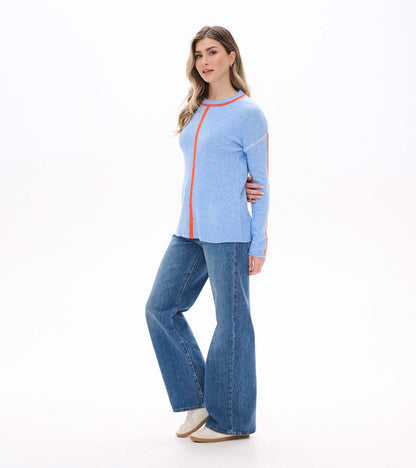 Side front view of azure blue Maeve sweater with orange center seam, sleeve stripes, and white shoulder stitching