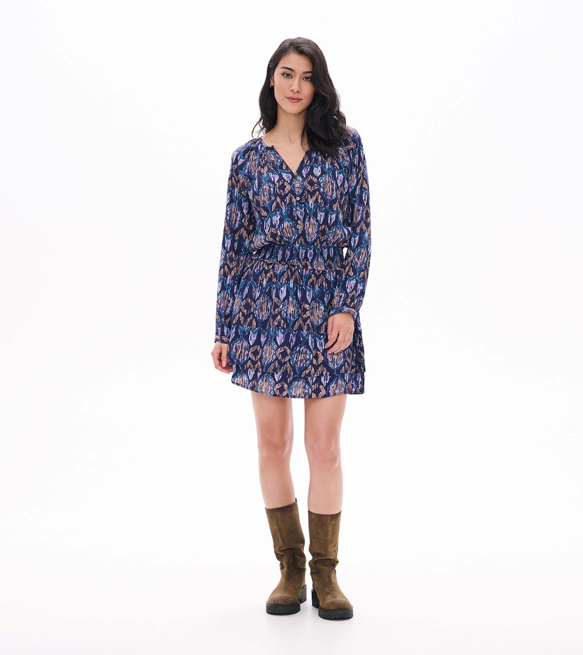 Front view of mini dress with long sleeves, smocked waist, buttoned V-neck and blue, purple and tan ikat print