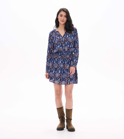 Front view of mini dress with long sleeves, smocked waist, buttoned V-neck and blue, purple and tan ikat print