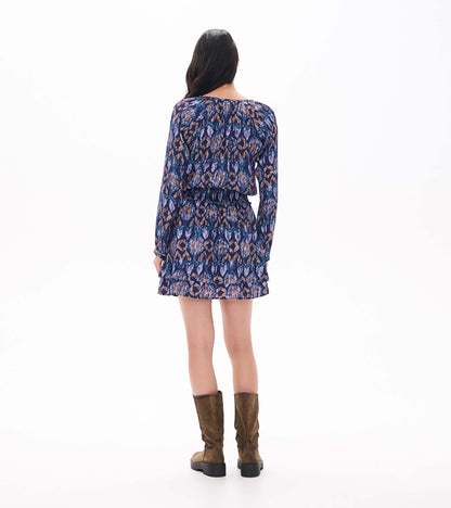 Back view of patterned mini dress with long sleeves, smocked waist, and tiered skirt