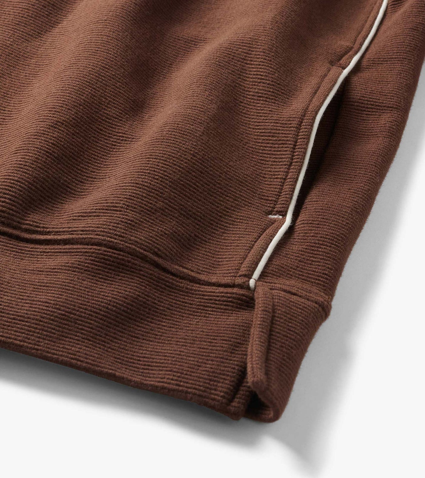 Close-up of brown 1/4 zip top with fine ribbed texture, white side piping, and hem detail