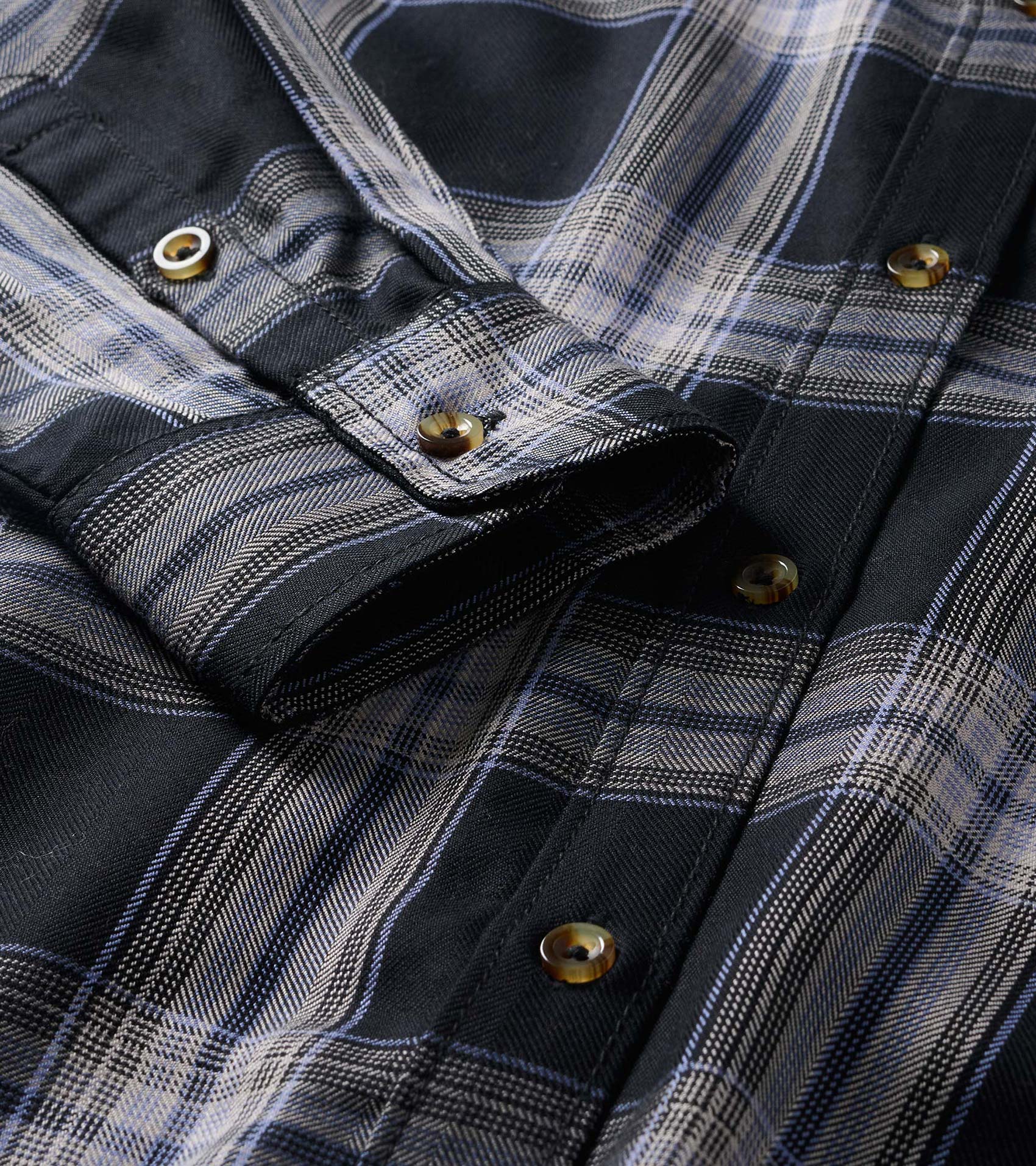 Close-up of black and tan plaid shirt dress showing button placket, collar, and rolled sleeve tab detail