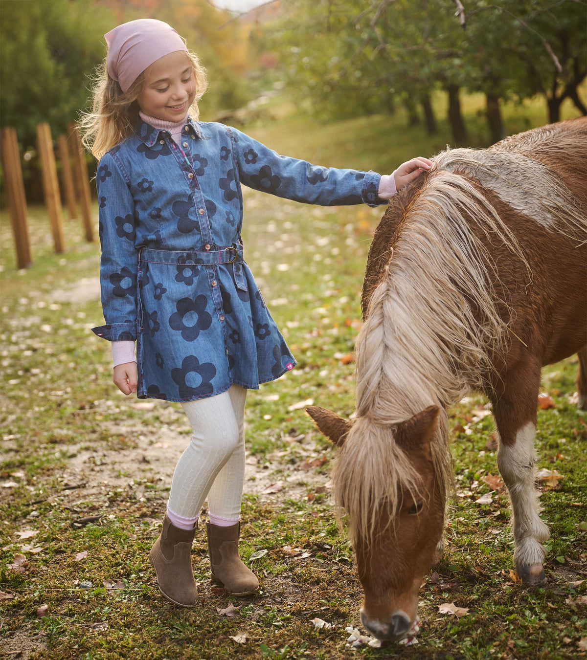 Girl wearing a blue flower-print belted shirt dress beside a pony in an outdoor setting