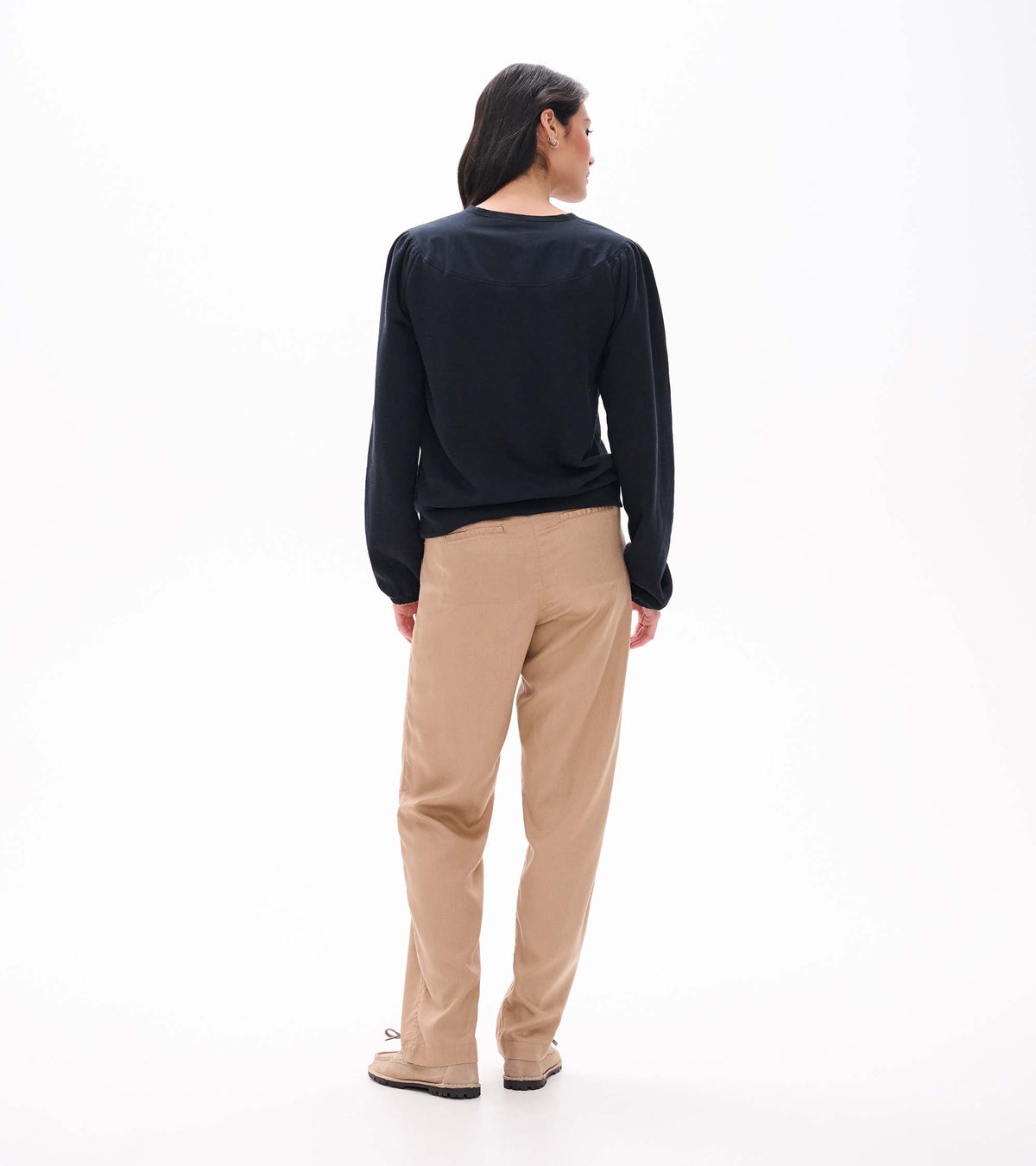 Back view of black long sleeve top with gathered shoulder seams and banded hem on model