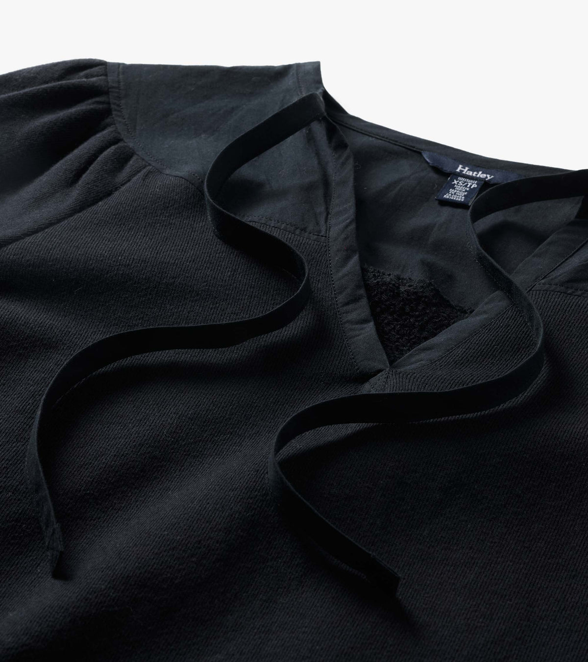 Close-up of black top with gathered shoulders, ribbed trim, V-neck opening, and long tie details