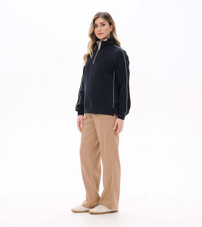 Black 1/4 zip knit top shown on model from front left angle with white sleeve piping