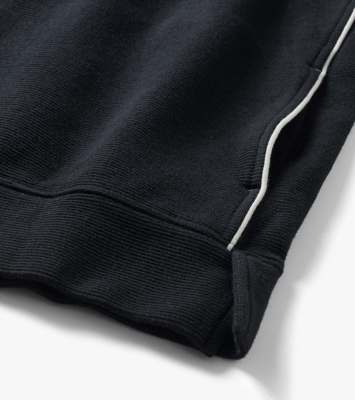 Close-up of black knit top hem and side seam with white piping detail