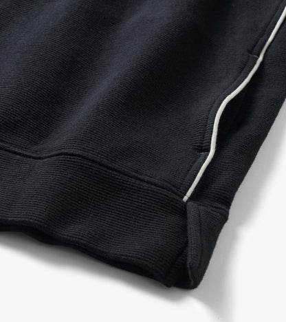 Close-up of black knit top hem and side seam with white piping detail