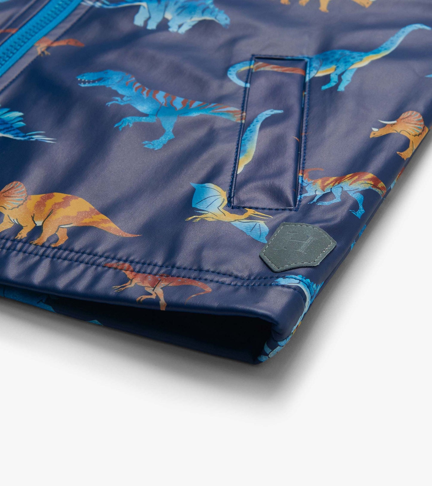 Close-up of lower front rain coat showing pocket flap, dinosaur print, and small gray shield patch