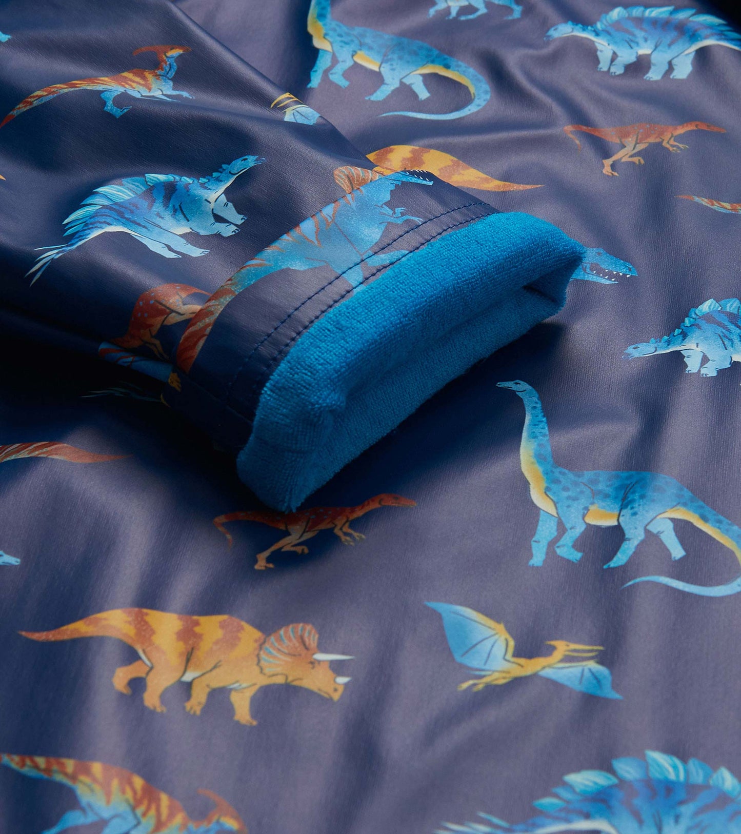 Close-up of blue rain coat fabric with colorful dinosaur print and bright blue cuff lining