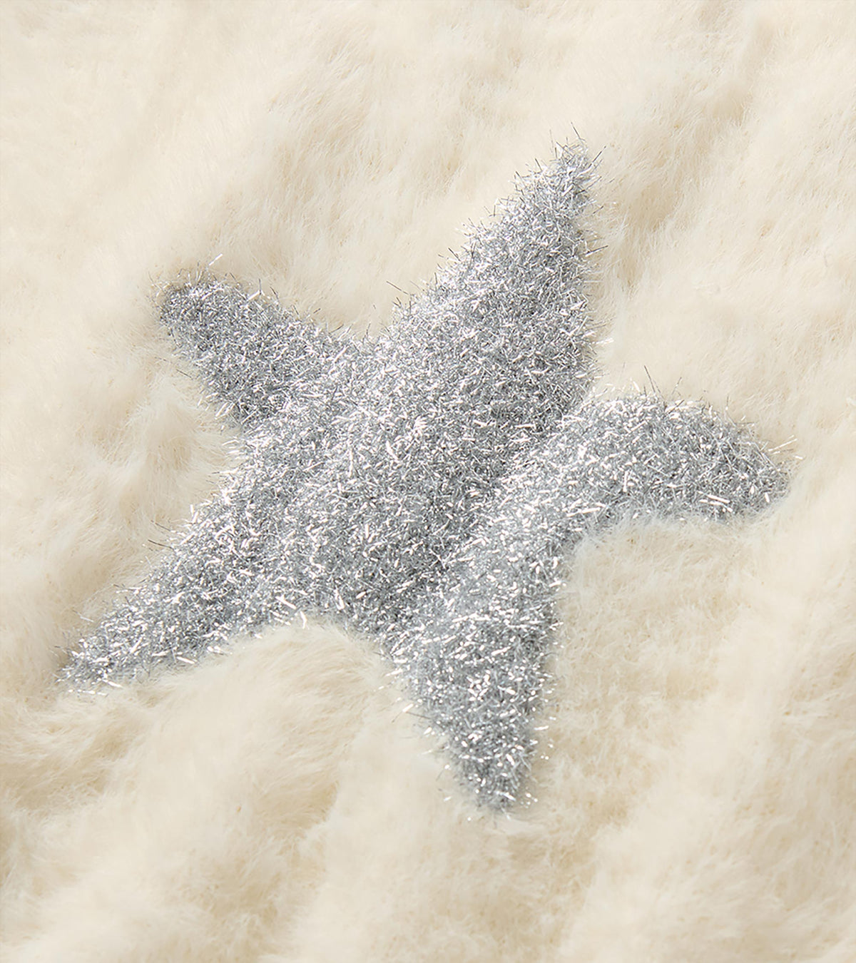 Close-up of silver star detail on cream fuzzy knit sweater vest