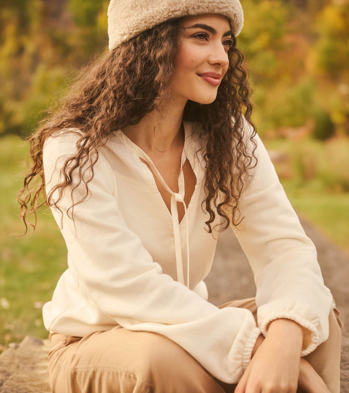 Cream long sleeve top with tie neckline and gathered cuffs, worn outdoors in a seated side view