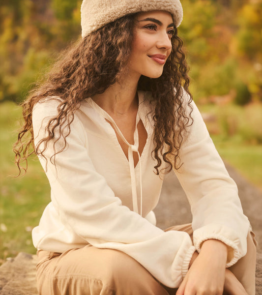 Cream long sleeve top with tie neckline and gathered cuffs, worn outdoors in a seated side view