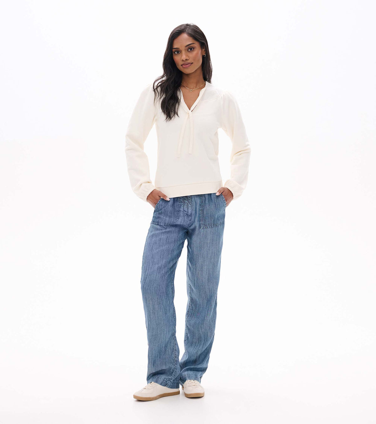 Full-length front view of cream tie-neck top with gathered cuffs, styled with wide leg blue pants