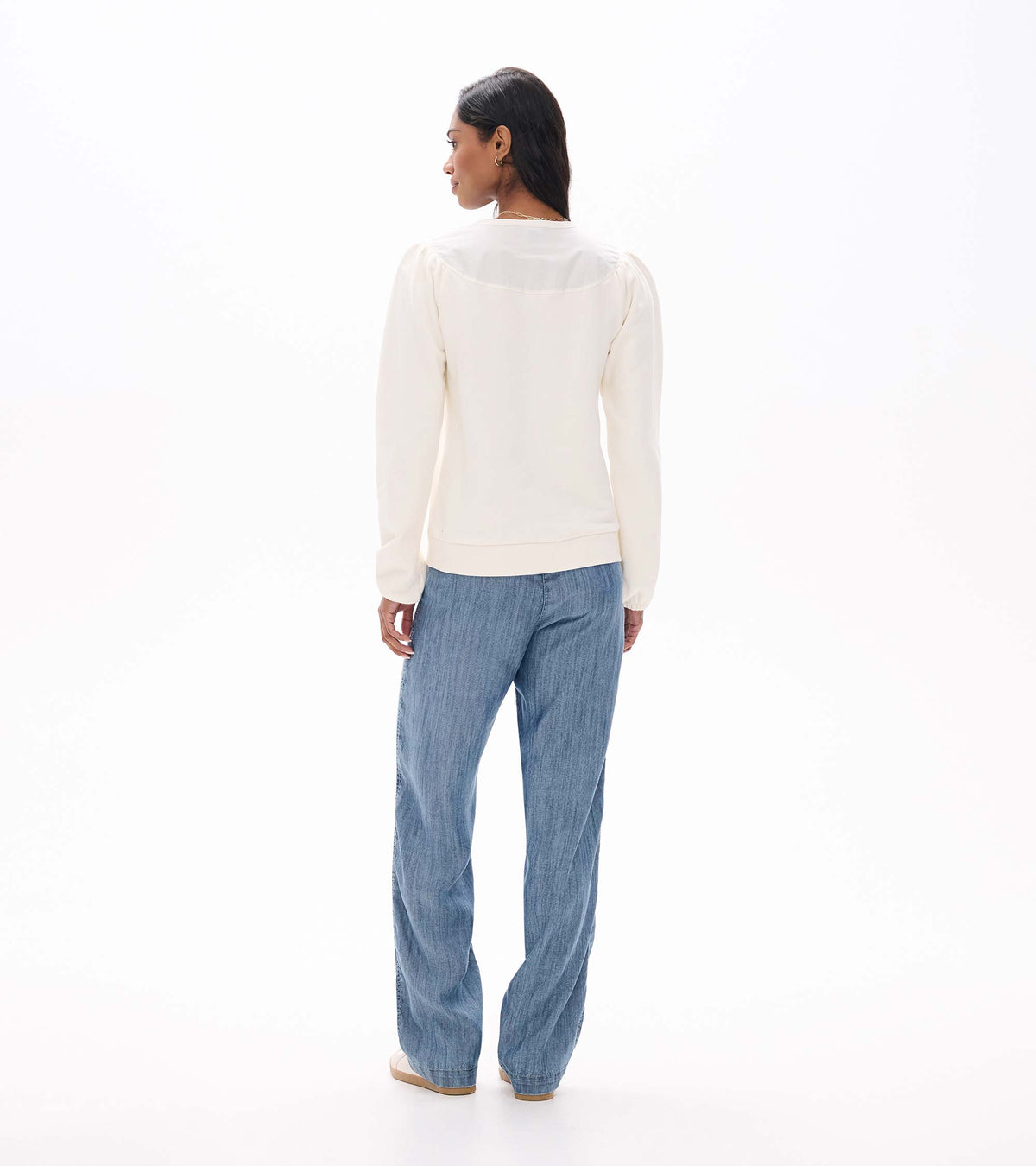 Back view of cream long sleeve top with gathered shoulders and curved back yoke, worn with light blue jeans