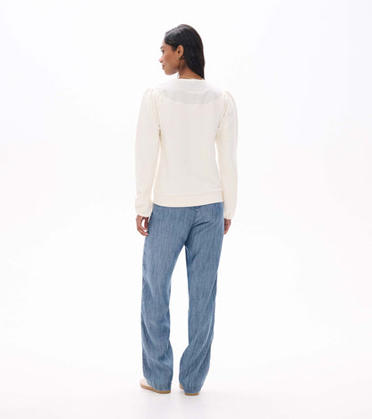 Back view of cream long sleeve top with gathered shoulders and curved back yoke, worn with light blue jeans