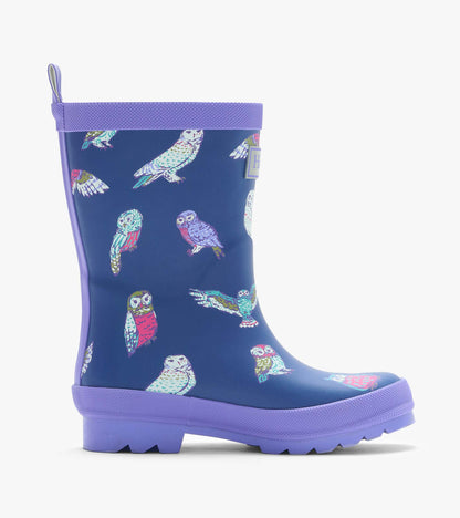 Side view of a navy kids rain boot with colorful owl print, purple trim, and treaded sole