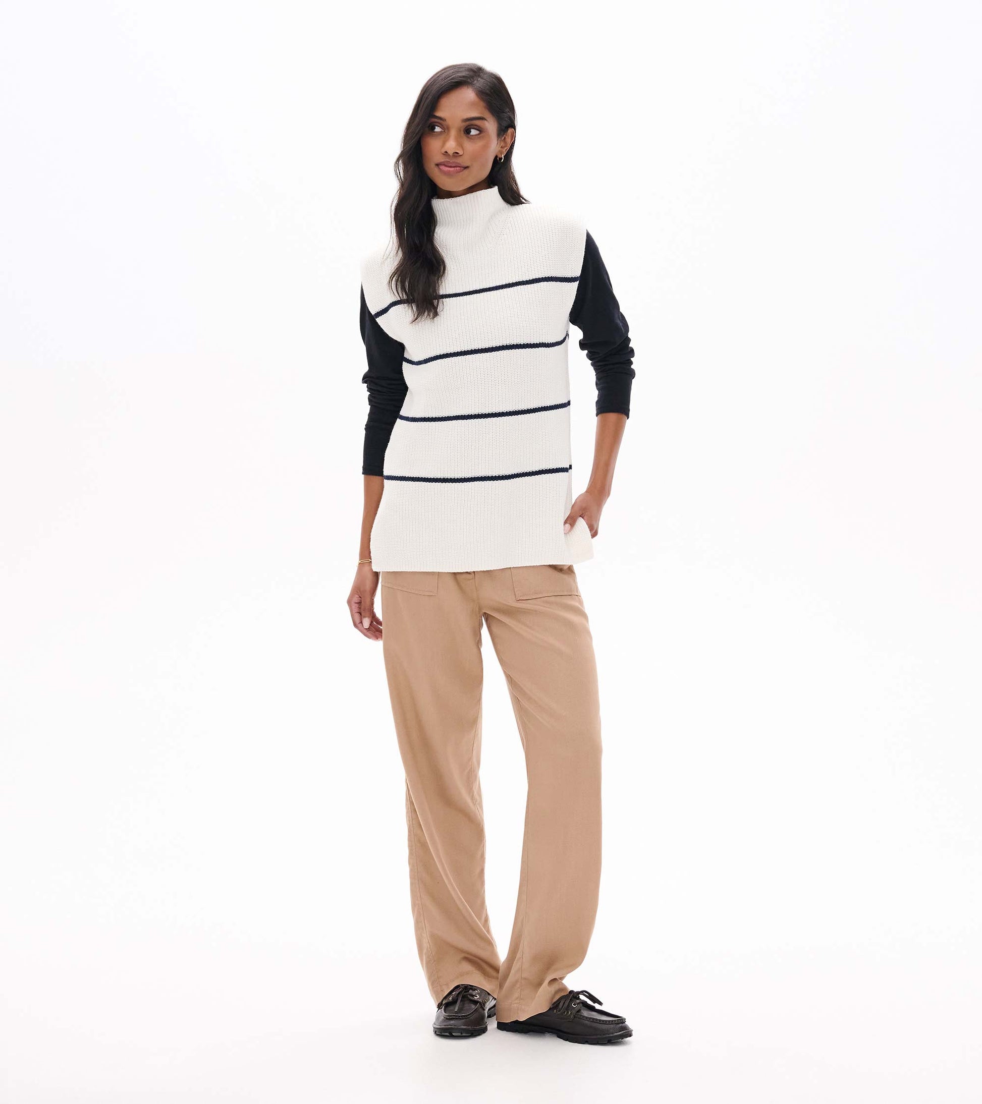 Cream sleeveless striped sweater tunic layered over a black long sleeve top, front view