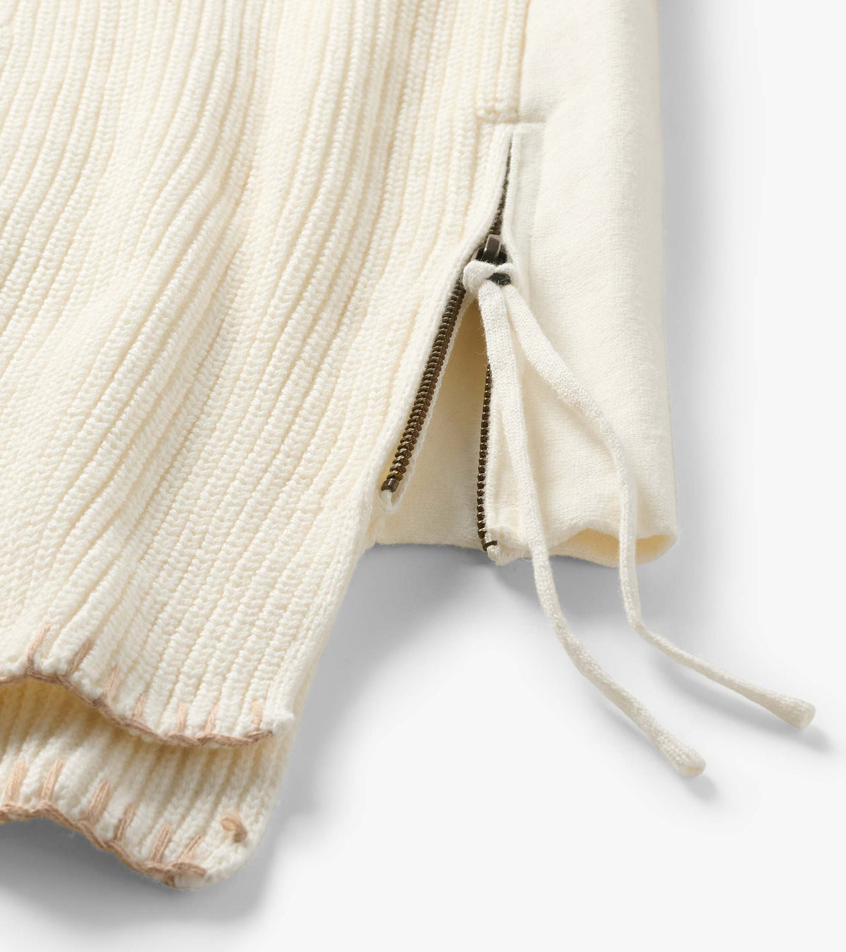 Close-up of cream sweater side hem with exposed zipper and long knit zipper pull detail
