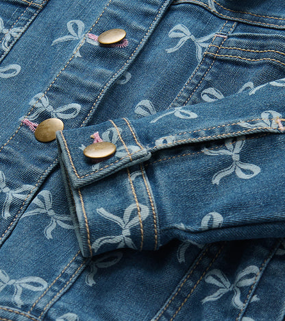 Close-up of blue bow-print denim jacket showing brass-tone buttons, cuff tab, and chest pocket detail