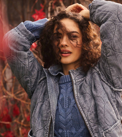 Close-up of blue acid-rinse quilted jacket with mock neck, shown over a blue cable-knit sweater