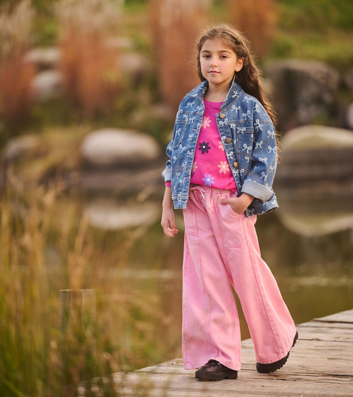 Girl wearing flamingo pink wide leg jeans with a denim jacket on a wooden walkway