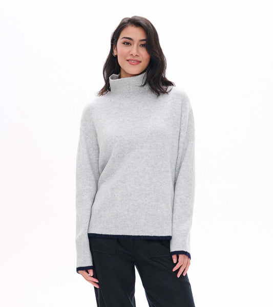 Model wearing athletic grey mock neck sweater with ribbed collar, hem, and cuffs with dark contrast trim