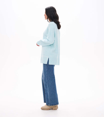 Side view of teal tunic sweater with drop shoulders, ribbed hem, and side slit